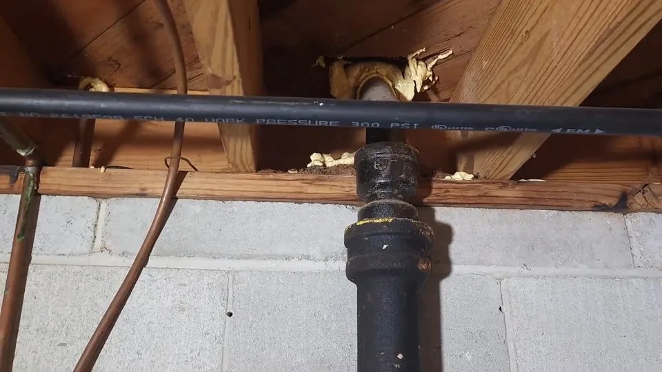 Black iron pipe running along basement joists above a block wall, beside copper lines