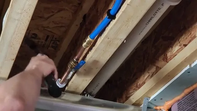 Hand tightening a fitting on a blue PEX line run through floor joists