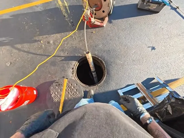 Inspection camera cable feeding into a cleanout set in paving