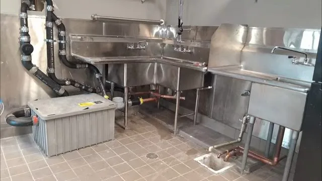 Stainless commercial kitchen sinks with a gray grease trap on the tile floor