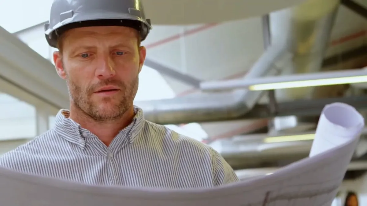Man in a hard hat studying a roll of plans inside an unfinished building