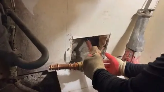 Gloved hands joining copper pipe at an opening cut in a wall