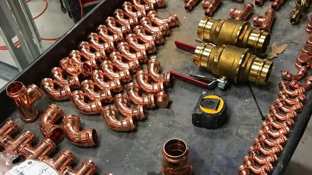Tray of copper elbows, brass valves and a tape measure laid out on a work surface
