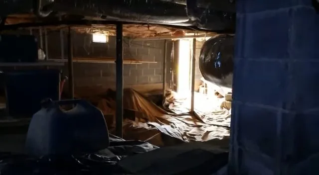 Crawl space with plastic vapor barrier laid over the soil and a dark tank at the back