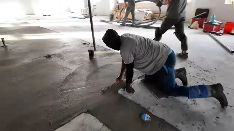 Worker kneeling on a concrete floor while others work behind him in an open commercial space