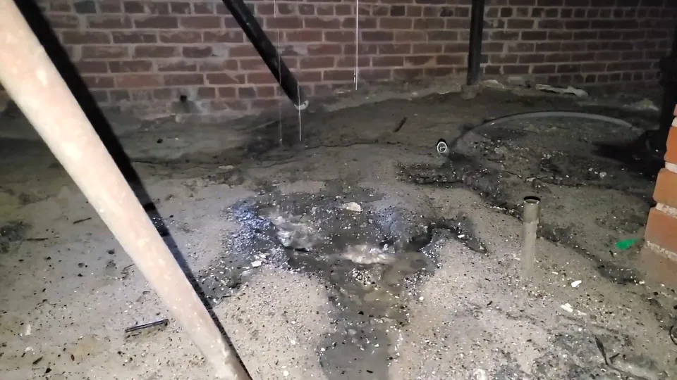 Damp concrete floor with debris beside a brick foundation wall