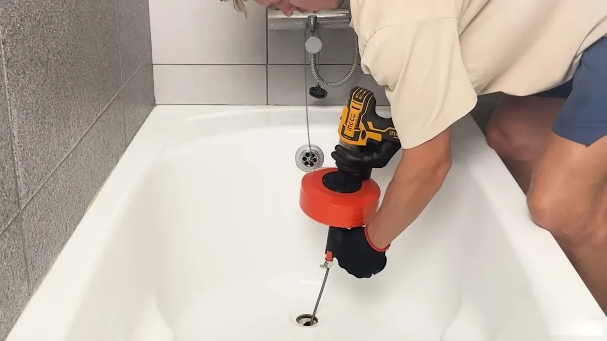Power drill driving a cable down a bathtub drain