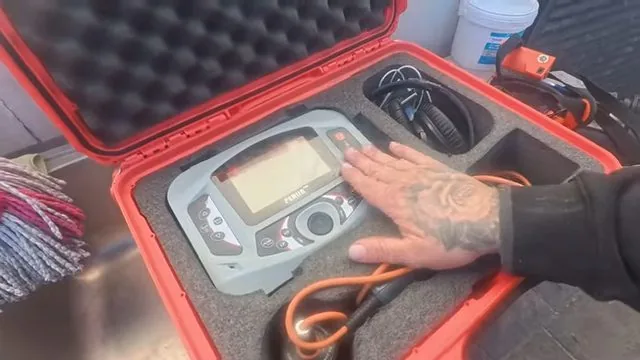 Handheld electronic detector in a red hard case with a hand resting on it