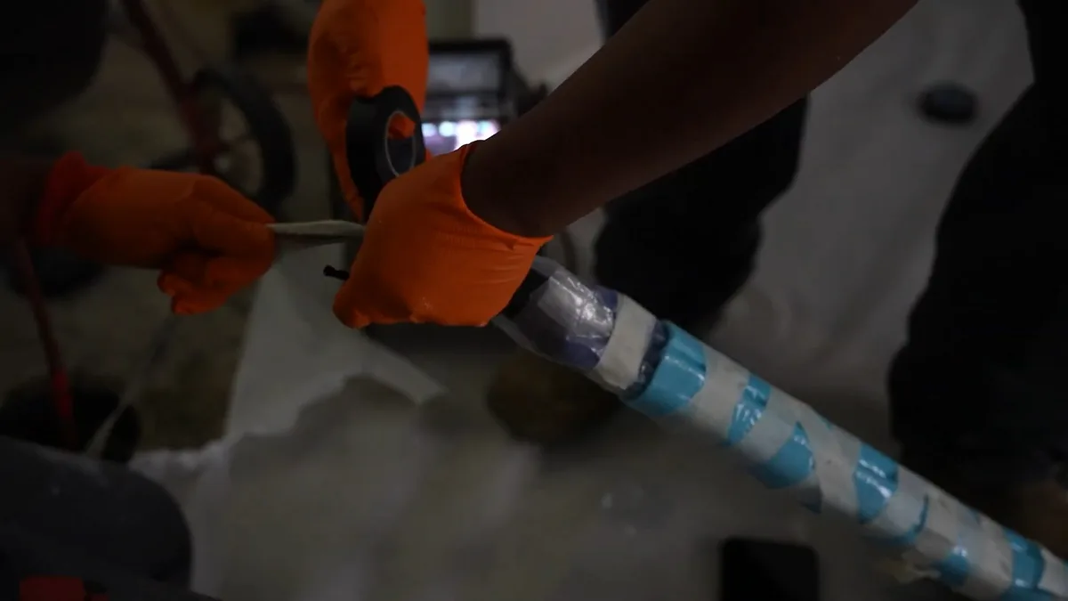 Gloved hands holding a pipe section with a blue lining inside