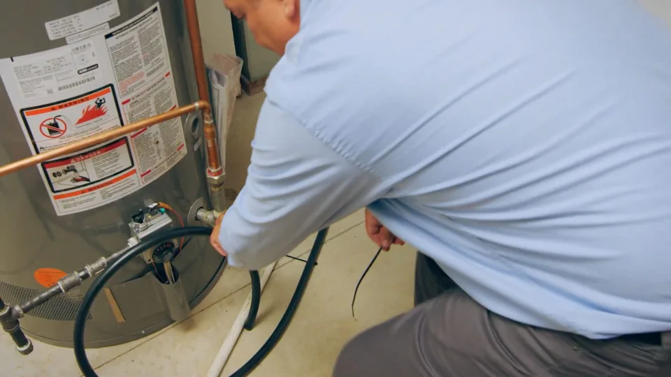 Man draining a water heater through a hose attached to the drain valve