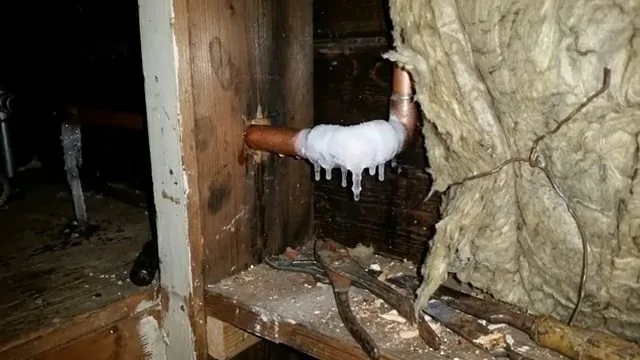 Copper elbow and pipe frosted with ice inside an exterior wall cavity
