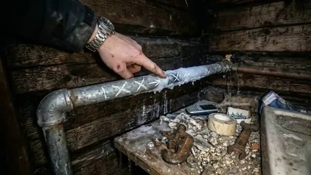 Frosted metal pipe marked with chalk in a dark crawlspace