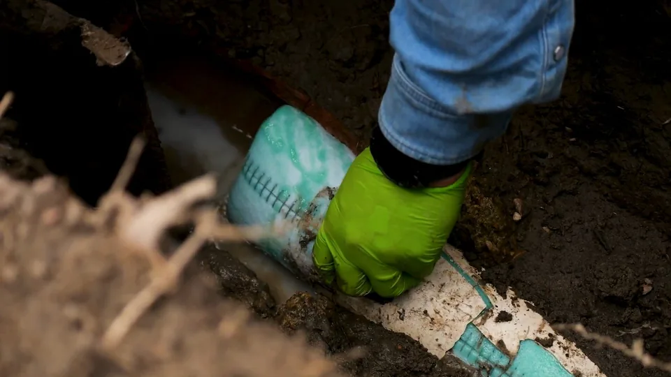 Gloved hand resting on PVC pipe at the bottom of a trench