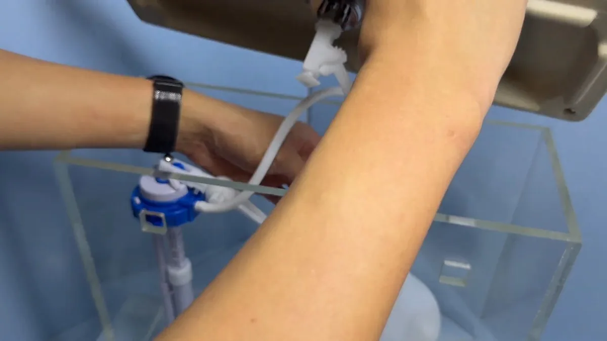 Hand adjusting the fill valve inside a clear toilet tank against a blue background