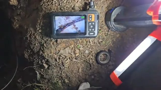 Handheld inspection monitor lying on soil beside a pipe at an excavation