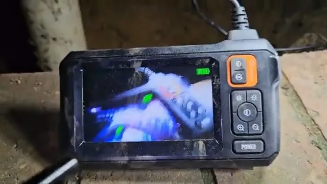Handheld inspection monitor with orange buttons held in a crawl space