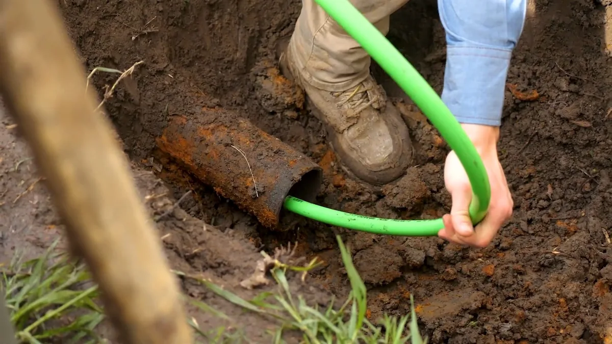 Green jetting hose fed into a broken pipe at the bottom of an excavation