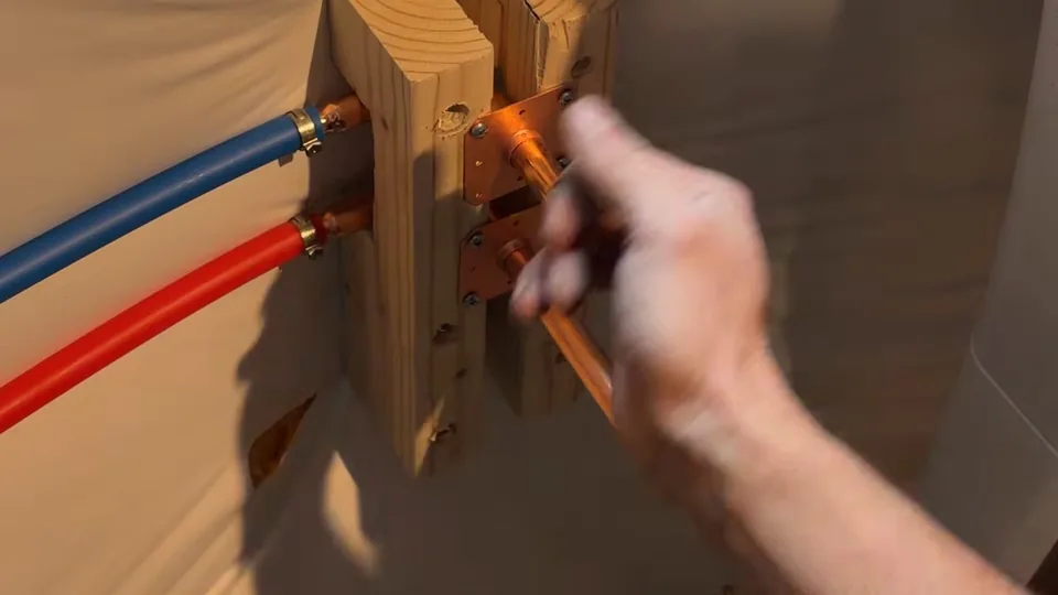 Red and blue PEX lines connected to copper stubs on a wood mounting block