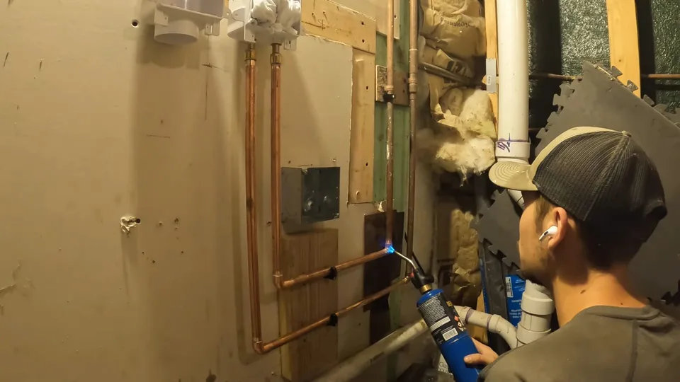 Plumber soldering a copper line on a wall beside a water heater