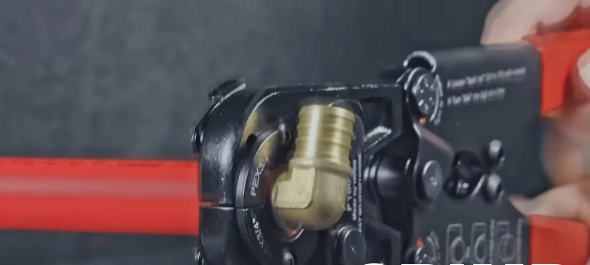 Press tool seating a brass elbow on a red PEX line