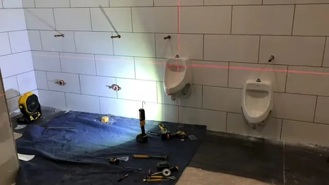 Two wall-hung urinals on a tiled wall with a laser level line across them