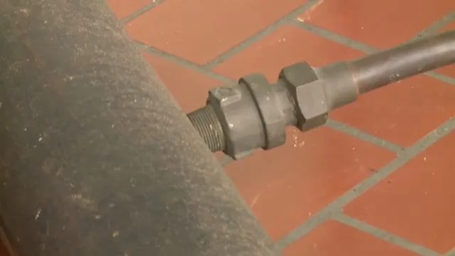 Threaded black iron union joining two sections of pipe beside a tiled floor