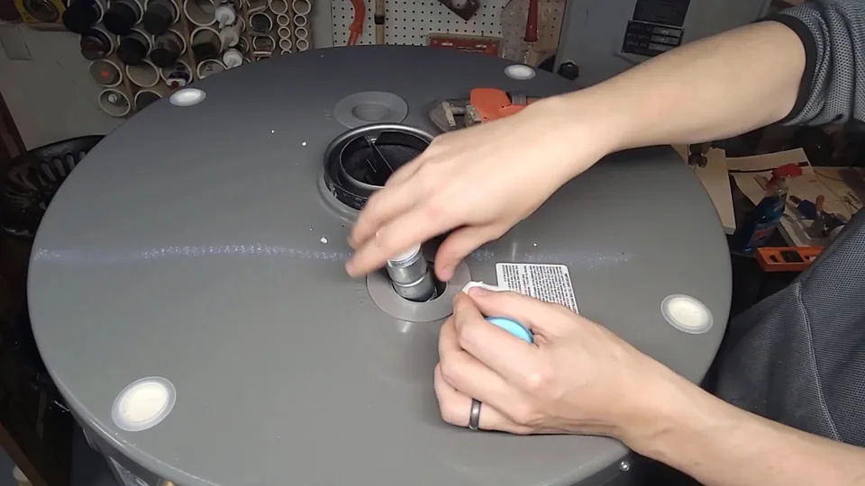 Hands working on a fitting at the top of a gray water heater