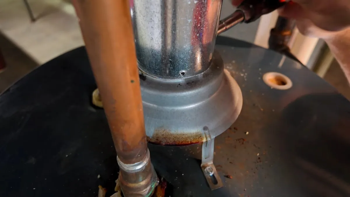 Water heater top with a flue collar, copper supply pipe and a hand holding a tool