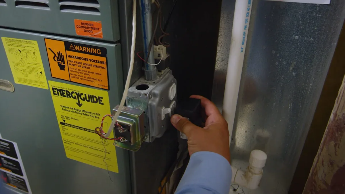 Hand beside the gas control valve and thermostat dial on a water heater