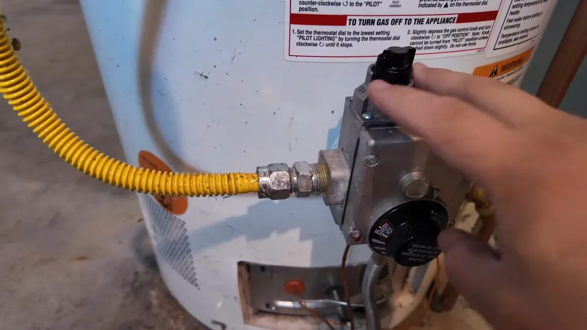 Hand on the gas control of a water heater with a yellow flexible gas line