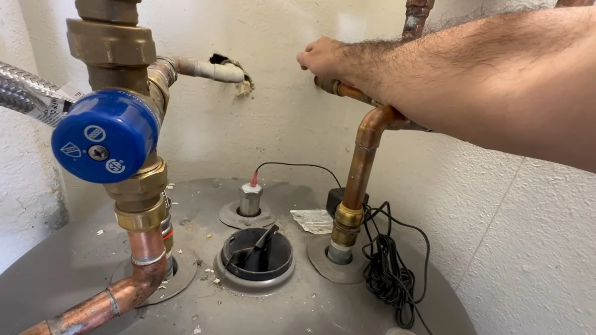 Arm reaching to copper pipe above a water heater with a blue valve handle and fittings