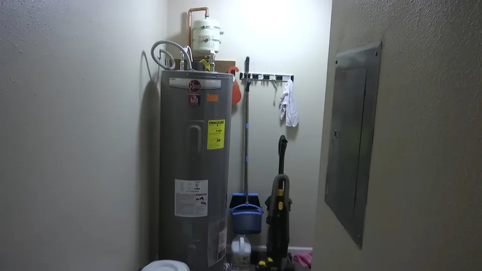 Tank water heater with a white expansion tank on top, standing in a utility closet