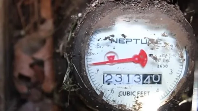 Water meter dial with a red sweep hand and soil-covered digits