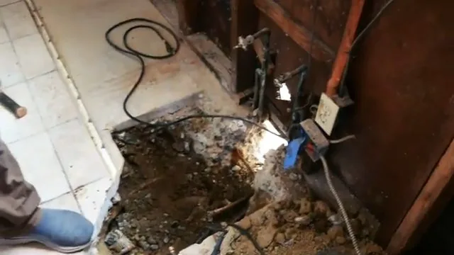 Demolished floor section with a power cord running across wet debris